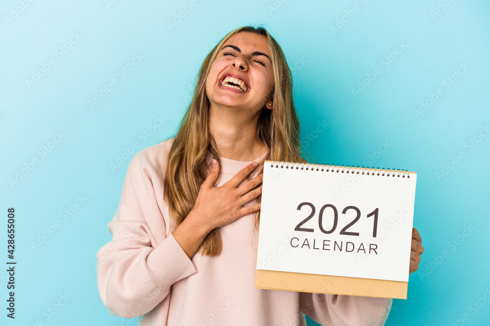 Young blonde caucasian woman holing a calendar isolated laughs out loudly keeping hand on chest. Young blonde caucasian woman holing a calendar isolated laughs out loudly keeping hand on chest.