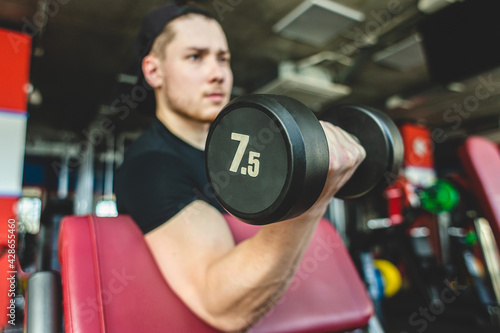 Portrait of a muscular man performs exercises in the gym. Strength training with dumbbells