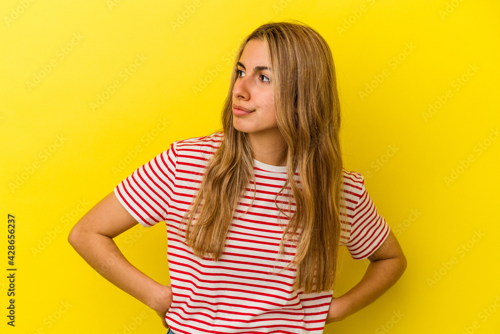 Young blonde caucasian woman isolated on yellow background looks aside smiling, cheerful and pleasant. Young blonde caucasian woman isolated on yellow background looks aside smiling, cheerful and pleasant.