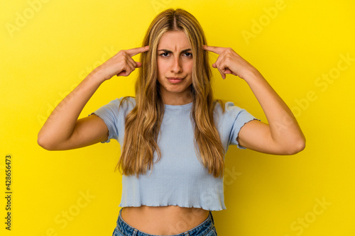 Young blonde caucasian woman isolated on yellow background focused on a task, keeping forefingers pointing head.