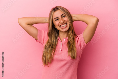 Young blonde caucasian woman isolated on pink background feeling confident, with hands behind the head.