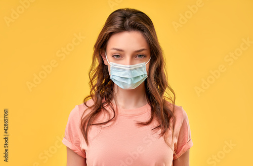 Beautiful girl in casual clothes and medical protective mask isolated on yellow background.