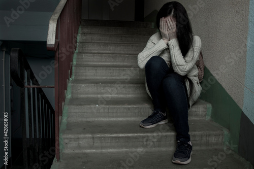 Sad girl sitting on the stairs at the entrance of the house