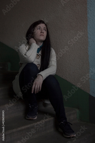 Sad girl sitting on the stairs at the entrance of the house