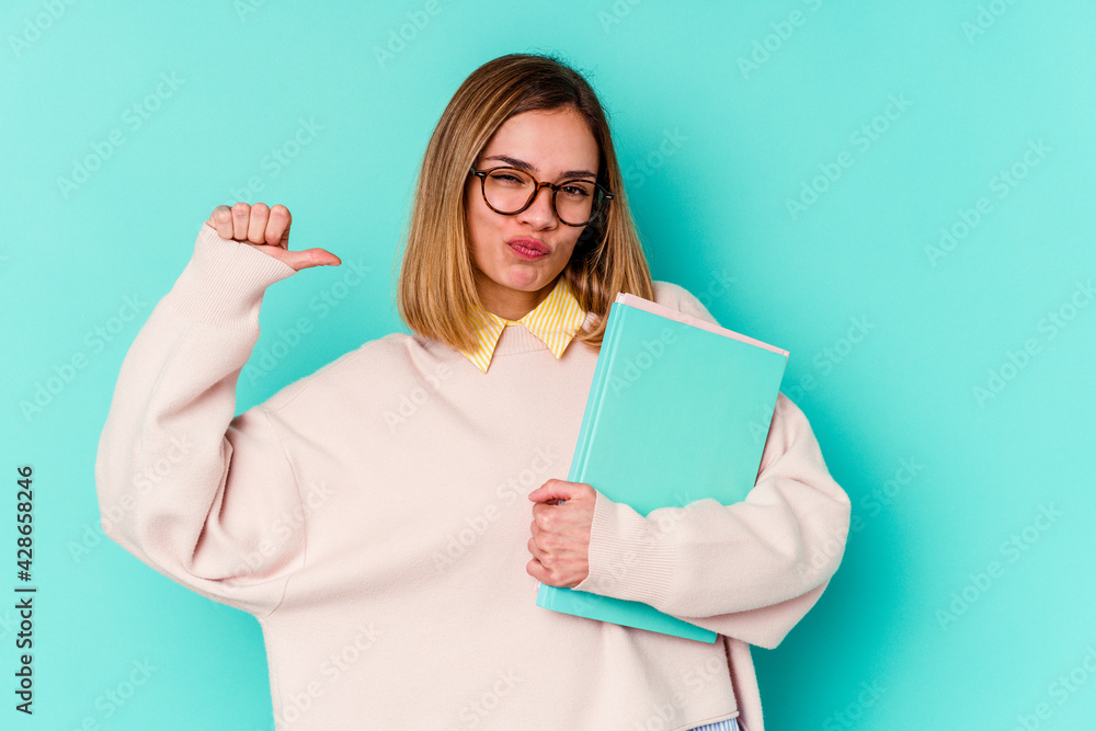 Young student woman holding books isolated on blue background feels proud and self confident, example to follow. Young student woman holding books isolated on blue background feels proud and self confident, example to follow.