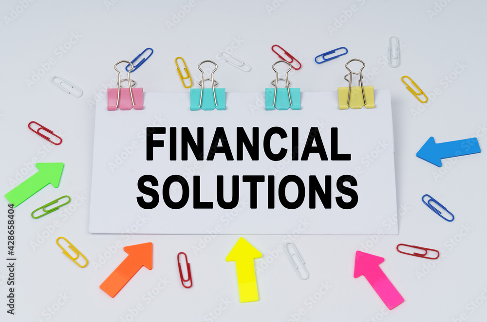On the table there are paper clips and directional arrows, a sign that says - FINANCIAL SOLUTIONS On the table there are paper clips and directional arrows, a sign that says - FINANCIAL SOLUTIONS