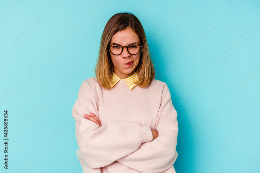 Young student caucasian woman isolated on blue background frowning face in displeasure, keeps arms folded. Young student caucasian woman isolated on blue background frowning face in displeasure, keeps arms folded.