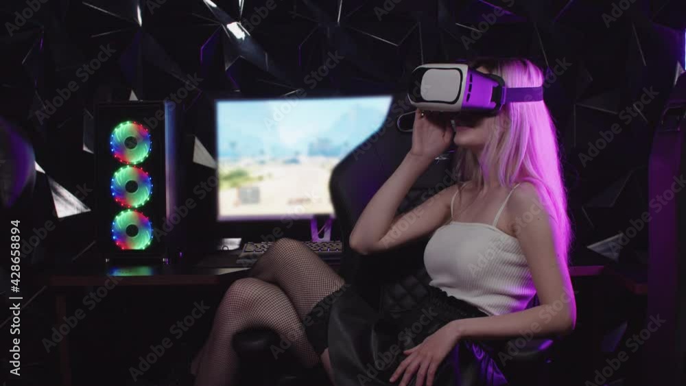 Young blonde gamer girl sitting in a chair wearing VR glasses Young blonde gamer girl sitting in a chair wearing VR glasses