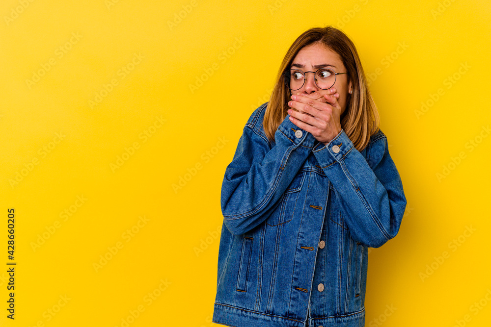 Young caucasian skinny woman isolated on yellow background thoughtful looking to a copy space covering mouth with hand. Young caucasian skinny woman isolated on yellow background thoughtful looking to a copy space covering mouth with hand.