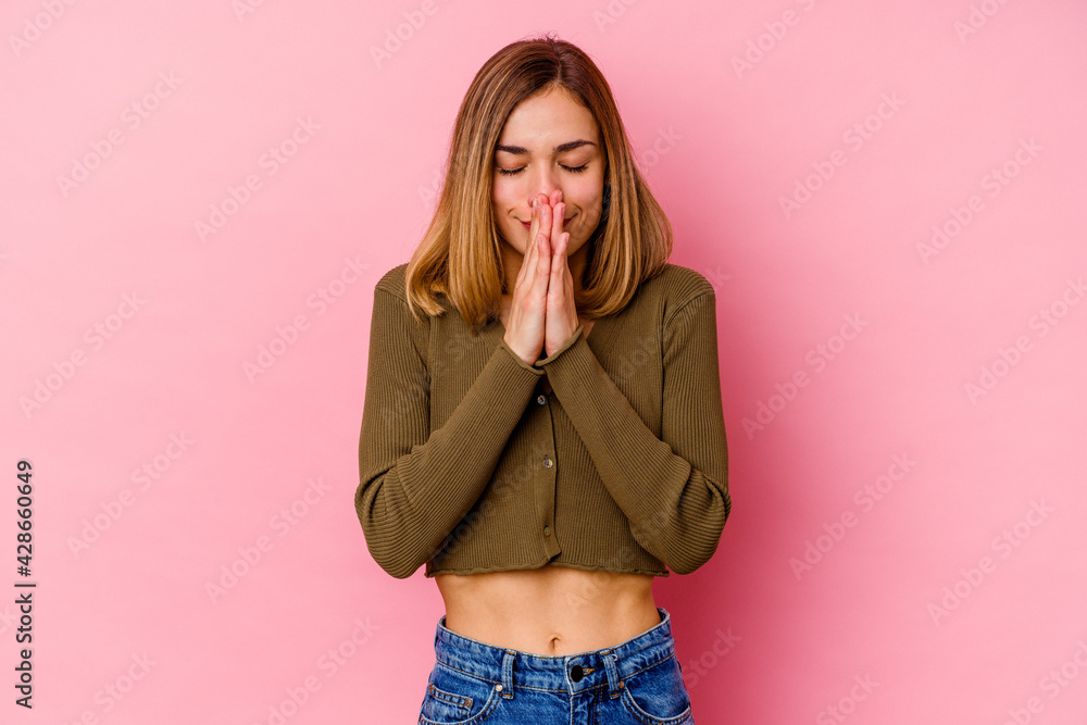Young caucasian woman isolated on pink background holding hands in pray near mouth, feels confident. Young caucasian woman isolated on pink background holding hands in pray near mouth, feels confident.