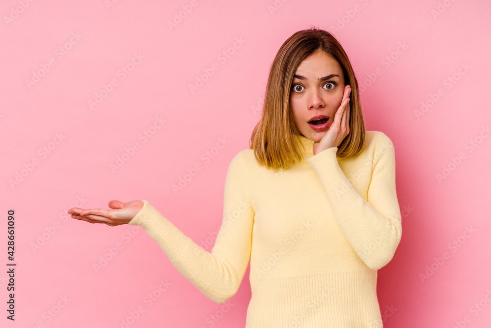Young caucasian woman isolated on pink background impressed holding copy space on palm. Young caucasian woman isolated on pink background impressed holding copy space on palm.