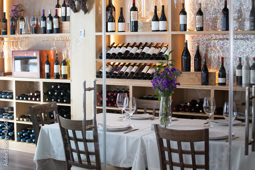 Restaurant table covered with a white cloth on the background of a regiment with bottles of wine. Empty restaurant with no people. Concept restaurateurs are waiting for customers. photo