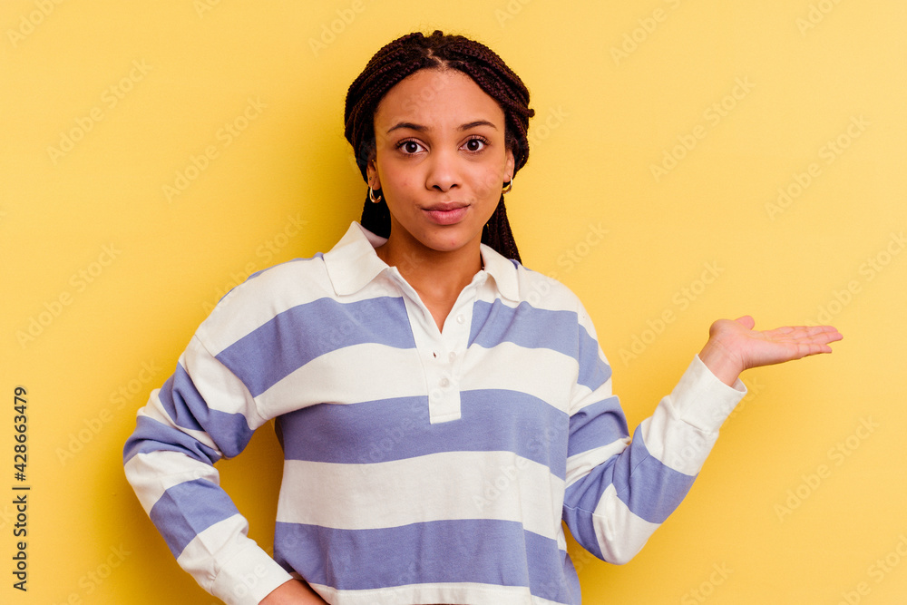 Young african american woman isolated on yellow background doubting and shrugging shoulders in questioning gesture.