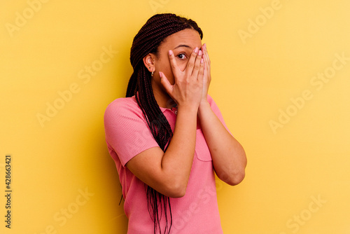 Young african american woman isolated on yellow background blink through fingers frightened and nervous. © Asier
