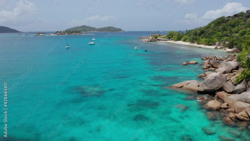 Aerial of tropical island with sail boats and sunny white sand beaches. Drone flies over turquoise blue ocean water and granite rocks of Seychelles, Africa. Gorgeous exotic paradise vacation landscape Aerial of tropical island with sail boats and sunny white sand beaches. Drone flies over turquoise blue ocean water and granite rocks of Seychelles, Africa. Gorgeous exotic paradise vacation landscape