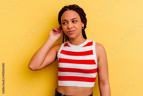 Young african american woman isolated on yellow background covering ears with fingers, stressed and desperate by a loudly ambient.
