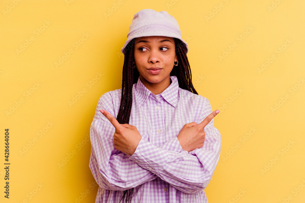 Young african american woman isolated on yellow background points sideways, is trying to choose between two options. Young african american woman isolated on yellow background points sideways, is trying to choose between two options.