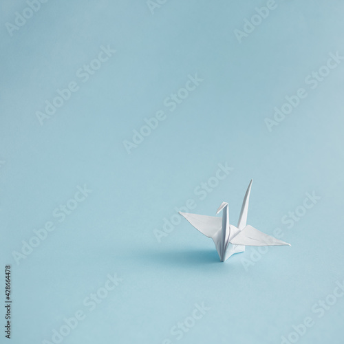 Minimalistic composition of a white origami crane. Orizuru on pastel blue background.