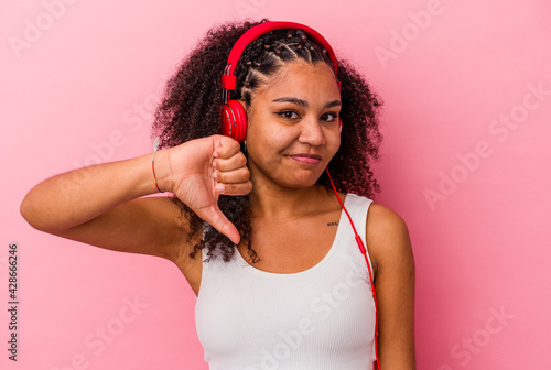 Young african american woman listening to music with headphones isolated on pink background showing a dislike gesture, thumbs down. Disagreement concept.