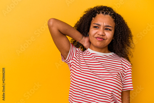 Young african american woman isolated on yellow background touching back of head, thinking and making a choice. © Asier