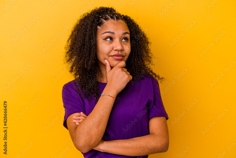 Young african american woman isolated on yellow background thinking and looking up, being reflective, contemplating, having a fantasy. Young african american woman isolated on yellow background thinking and looking up, being reflective, contemplating, having a fantasy.