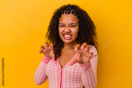 Young african american woman isolated on yellow background showing claws imitating a cat, aggressive gesture.