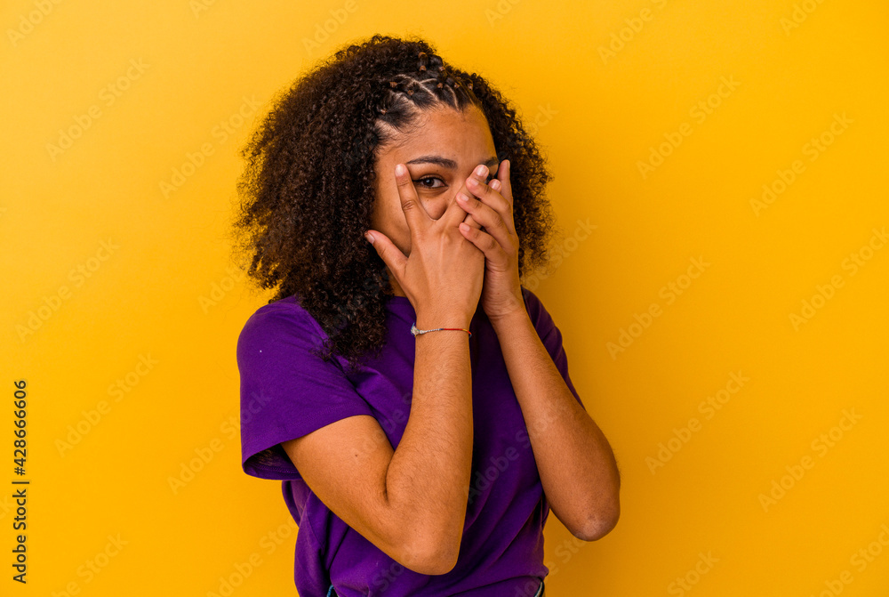 Young african american woman isolated on yellow background blink through fingers frightened and nervous. Young african american woman isolated on yellow background blink through fingers frightened and nervous.