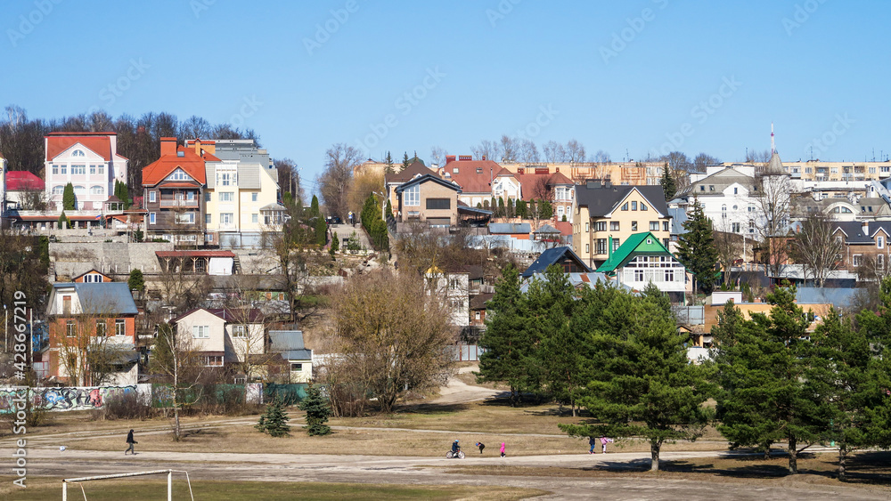 Village houses on a hill against a blue sky. Meadow with trees and grass in the field in front of the house. Horizontal village landscape with summer sunny day.