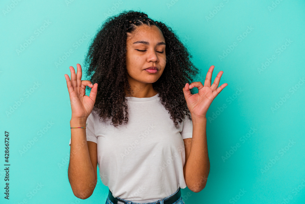 Young african american woman isolated on blue background relaxes after hard working day, she is performing yoga. Young african american woman isolated on blue background relaxes after hard working day, she is performing yoga.