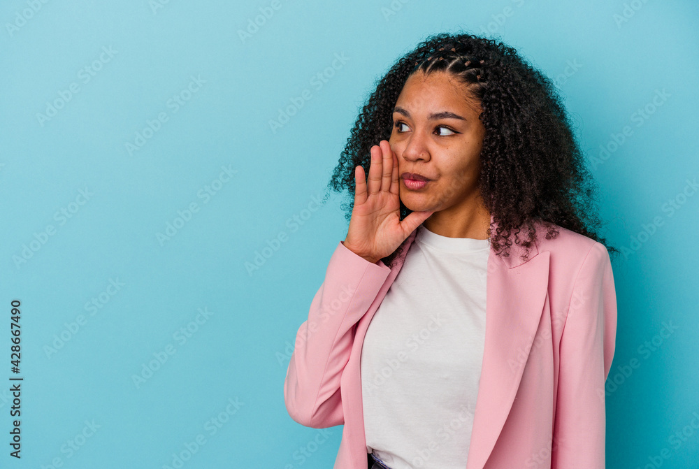 Young african american woman isolated on blue background is saying a secret hot braking news and looking aside