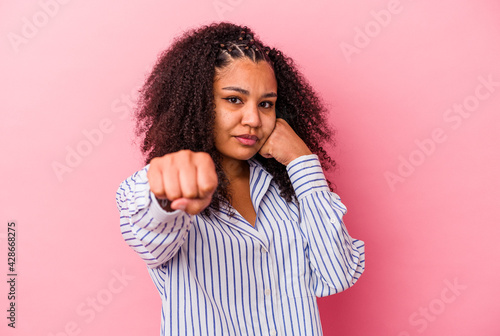Young african american woman isolated on pink background throwing a punch, anger, fighting due to an argument, boxing. © Asier