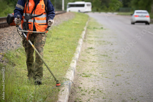 Closeup of a man with a lawn mower in his hands. A worker mows the grass on the side of the road. Improvement of the adjacent territory