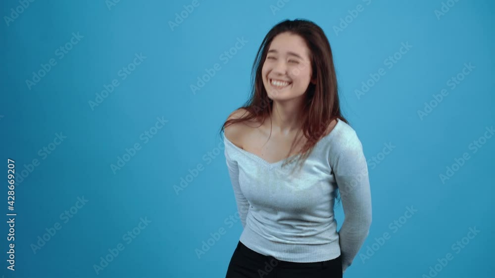 The optimistic young brunette displays a wide smile and laughs to tears. Asian with dark hair, dressed in a blue blouse, isolated on a dark blue background in the studio. The lifestyle concept of The optimistic young brunette displays a wide smile and laughs to tears. Asian with dark hair, dressed in a blue blouse, isolated on a dark blue background in the studio. The lifestyle concept of