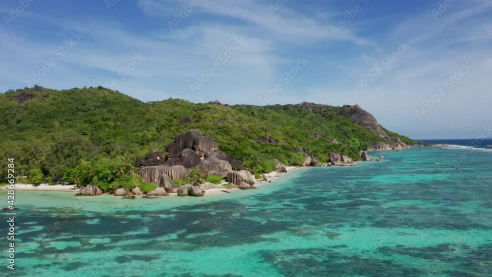 Aerial wide pan of sunny La Digue island, Seychelles. Anse source D’Argent paradise beach drone shot with turquoise blue water, white sand, palm trees and granite rocks. Adventure vacation destination Aerial wide pan of sunny La Digue island, Seychelles. Anse source D’Argent paradise beach drone shot with turquoise blue water, white sand, palm trees and granite rocks. Adventure vacation destination