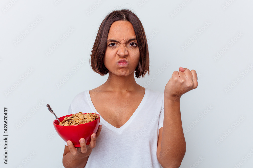 Young mixed race woman eating cereals isolated on white background showing fist to camera, aggressive facial expression. Young mixed race woman eating cereals isolated on white background showing fist to camera, aggressive facial expression.