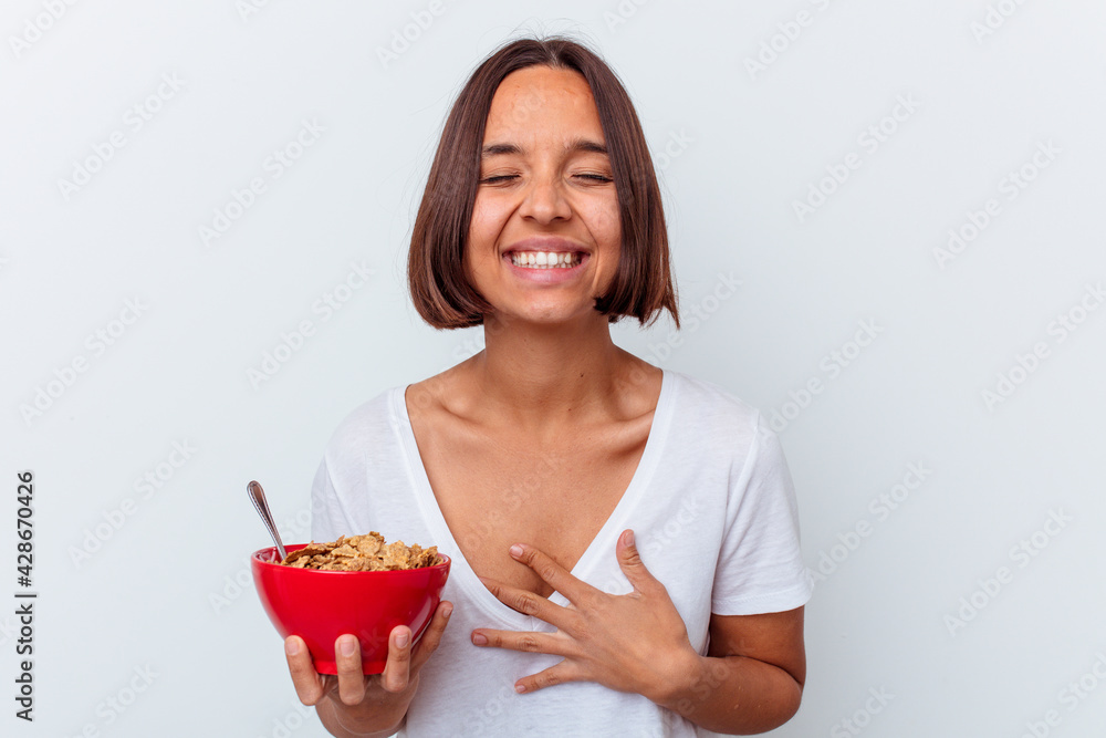 Young mixed race woman eating cereals isolated on white background laughing and having fun. Young mixed race woman eating cereals isolated on white background laughing and having fun.