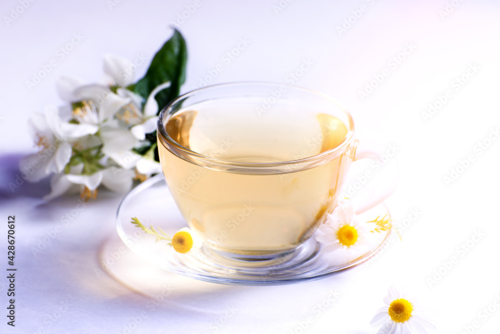 Cup of hot herbal tea with chamomile flowers against a light background. Cup of hot herbal tea with chamomile flowers against a light background.