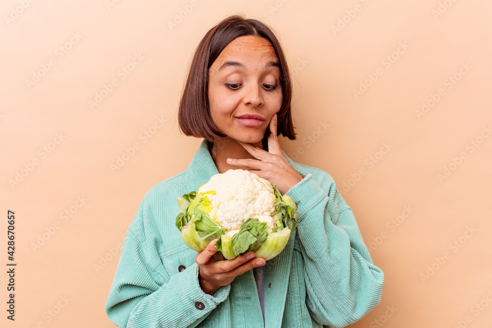 Young mixed race woman holding a cabbage isolated on beige background Young mixed race woman holding a cabbage isolated on beige background