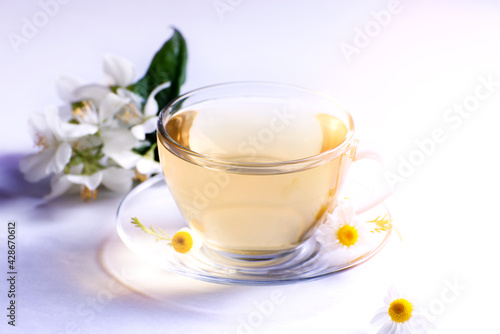 Cup of hot herbal tea with chamomile flowers against a light background.