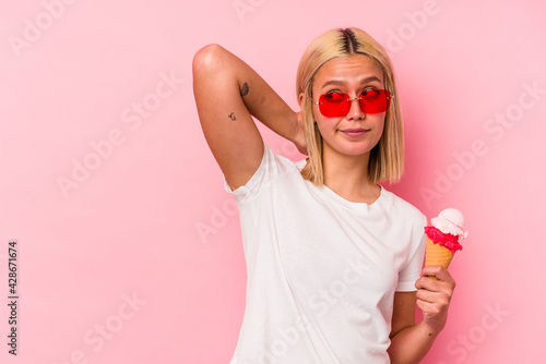 Young venezuelan woman eating an ice cream isolated on pink background touching back of head, thinking and making a choice.