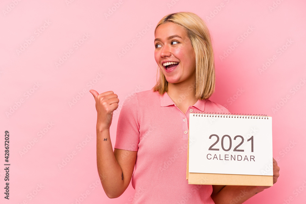 Young venezuelan woman holding a calendar isolated on pink background points with thumb finger away, laughing and carefree. Young venezuelan woman holding a calendar isolated on pink background points with thumb finger away, laughing and carefree.