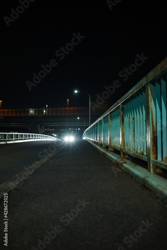 夜の橋・近づいてくる自動車のヘッドライトと錆びた欄干