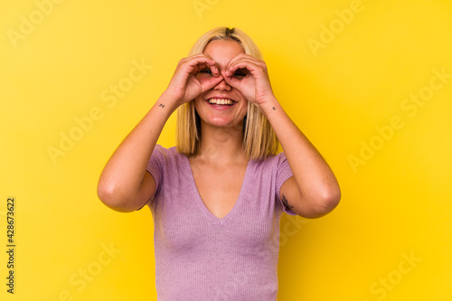 Young venezuelan woman isolated on yellow background showing okay sign over eyes