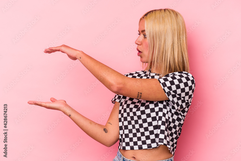 Young venezuelan woman isolated on pink background shocked and amazed holding a copy space between hands. Young venezuelan woman isolated on pink background shocked and amazed holding a copy space between hands.