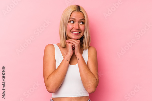Young venezuelan woman isolated on pink background keeps hands under chin, is looking happily aside.