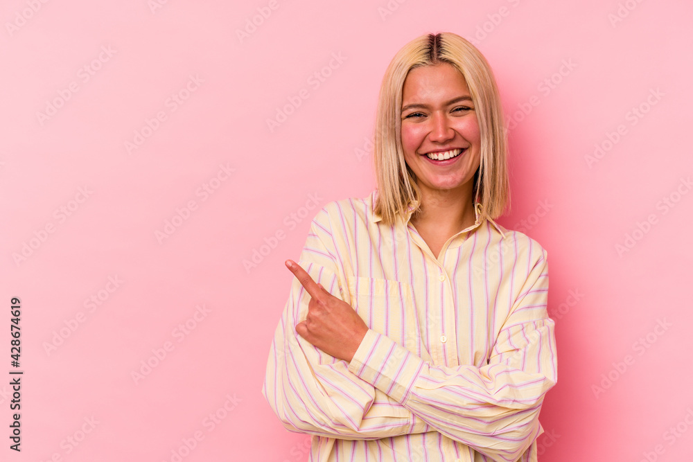 Young venezuelan woman isolated on pink background smiling cheerfully pointing with forefinger away.