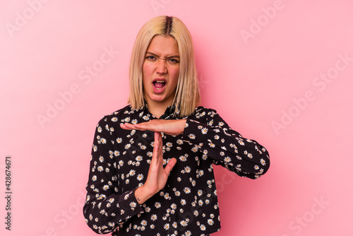 Young venezuelan woman isolated on pink background showing a timeout gesture. © Asier