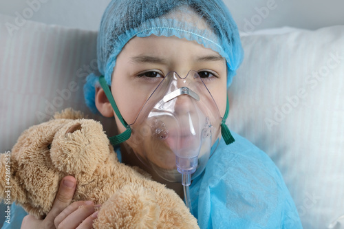 little patient in shirt, child, boy lies with teddy bear, facial oxygen mask, concept of medical care, anesthesiology and intensive care, oxygen therapy, treatment of coronavirus, COVID-19 photo