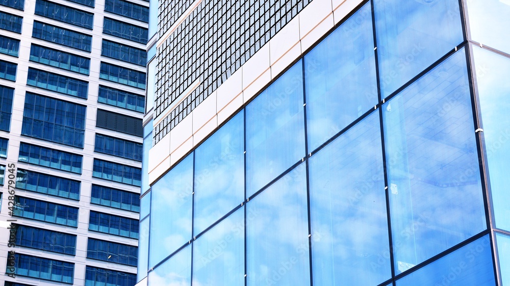 Abstract closeup of the glass-clad facade of a modern building covered in reflective plate glass. Architecture abstract background. Glass wall and facade detail. Velvia graphic filter. Abstract closeup of the glass-clad facade of a modern building covered in reflective plate glass. Architecture abstract background. Glass wall and facade detail. Velvia graphic filter.