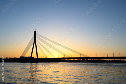 Scenic view of long cable-stayed bridge silhouette over the river at sunset.